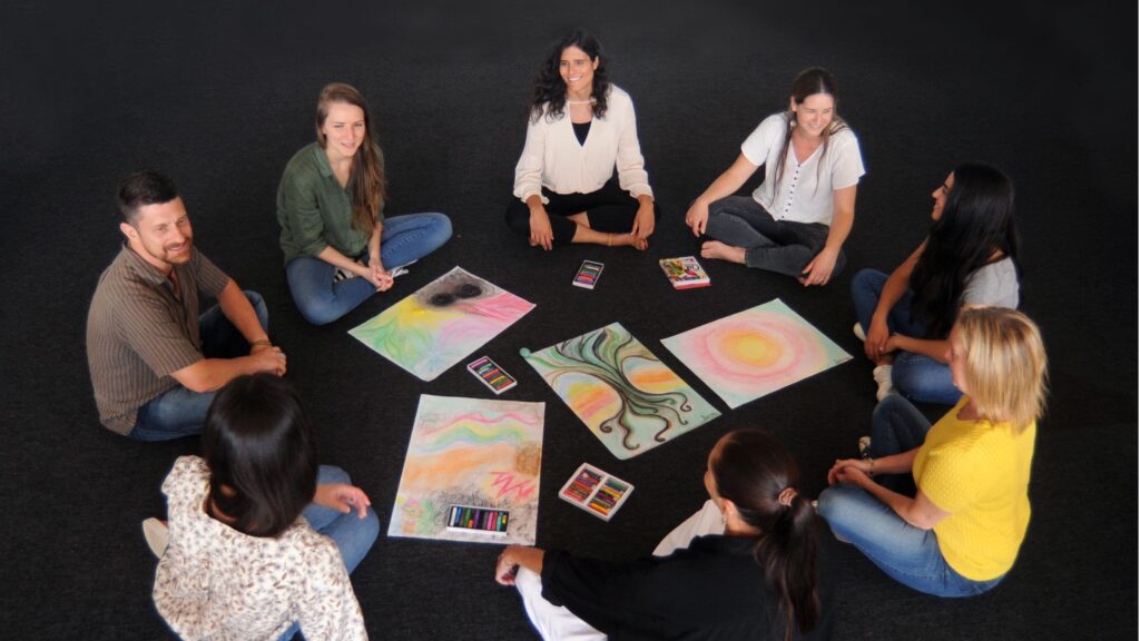 A group of Advanced Diploma of Transpersonal Therapy sitting in a circle with their artwork.