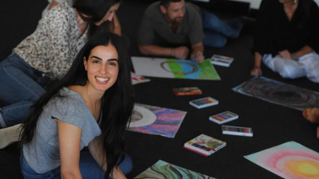 A smiling student in a group session site on the floor surrounded by art and drawings.