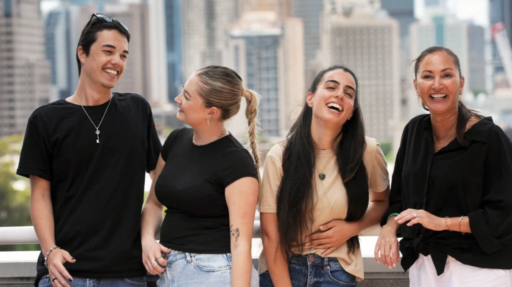 A group of CCM students enjoying a laugh while standing on a balcony with the CBD in the background.